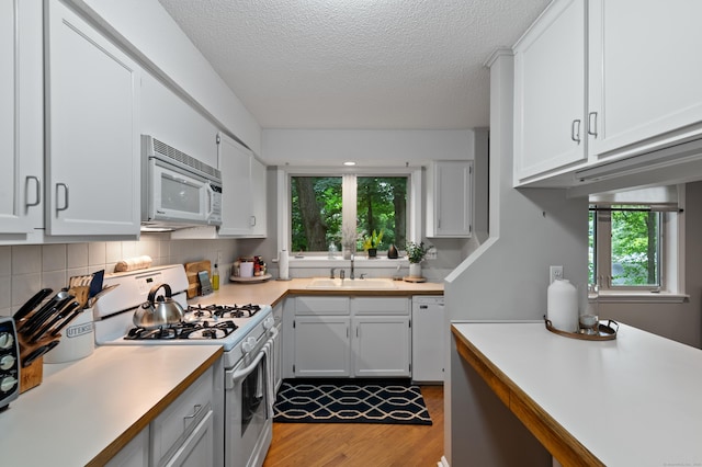 kitchen with white appliances, light wood-style flooring, light countertops, a sink, and plenty of natural light