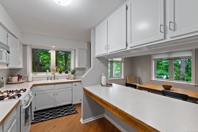 kitchen featuring a sink, white appliances, light wood finished floors, light countertops, and white cabinets