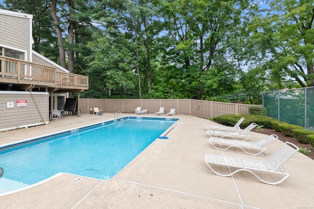 community pool featuring view of wooded area and a patio area