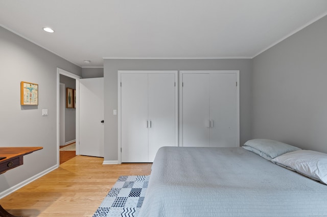bedroom featuring two closets, light wood-style floors, ornamental molding, recessed lighting, and baseboards