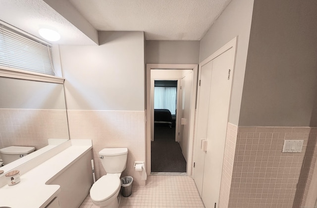 bathroom featuring tile walls, tile patterned flooring, toilet, wainscoting, and a textured ceiling