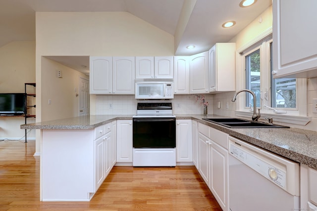 kitchen with white appliances, a sink, vaulted ceiling, a peninsula, and white cabinets