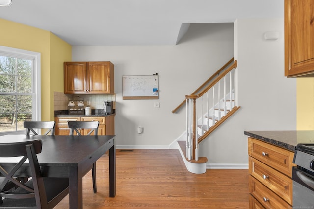 kitchen with light wood-style flooring, range, dark countertops, tasteful backsplash, and brown cabinets