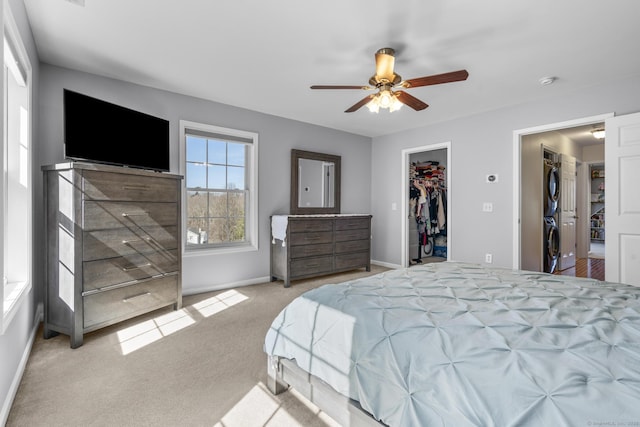 carpeted bedroom with stacked washing machine and dryer, a spacious closet, baseboards, ceiling fan, and a closet