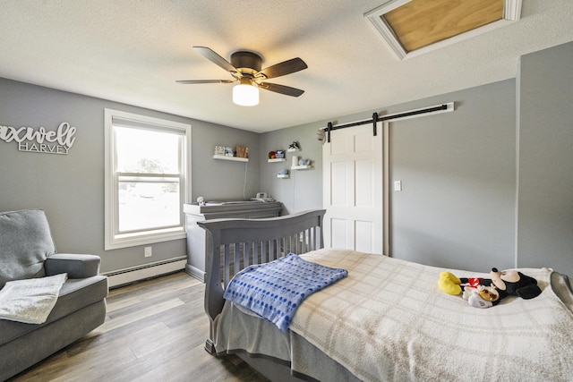 49 First Ave, Enfield, CT 06082 - bedroom featuring a baseboard heating unit, wood finished floors, a barn door, a ceiling fan, and a textured ceiling