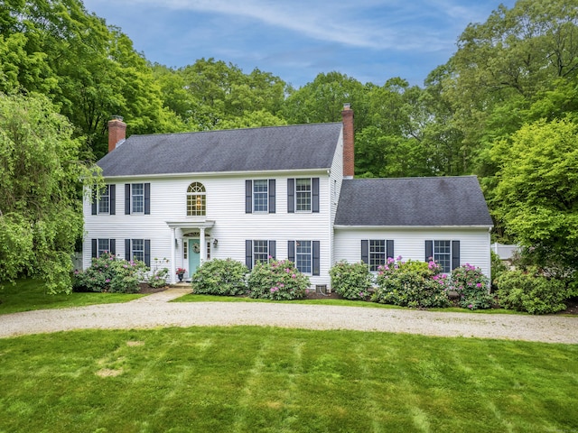 colonial home featuring a chimney, a front yard, and a shingled roof