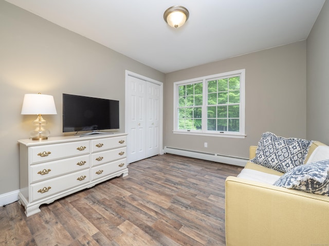 living area with a baseboard heating unit, wood finished floors, and baseboards