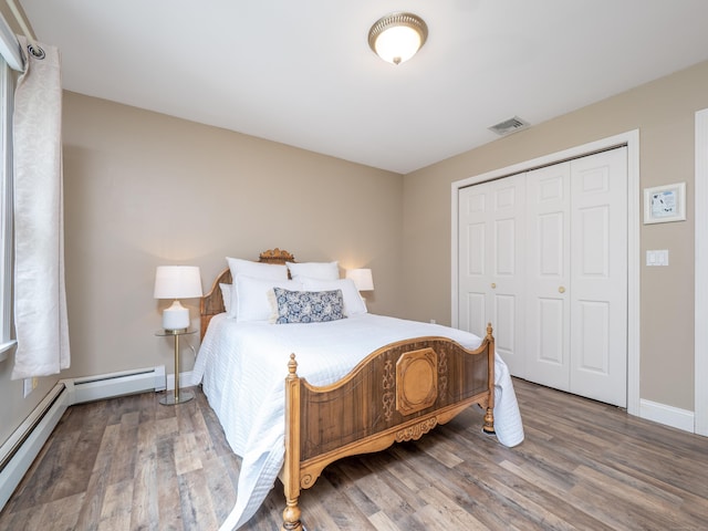 bedroom featuring wood finished floors, a closet, baseboards, and baseboard heating
