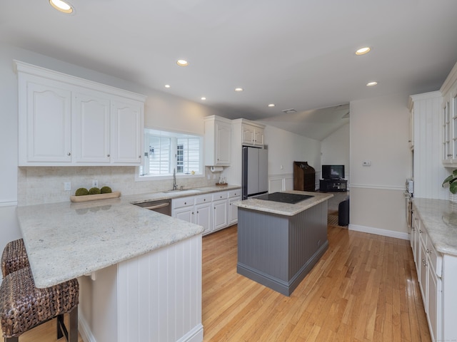 kitchen with appliances with stainless steel finishes, white cabinets, a peninsula, light wood-style floors, and backsplash