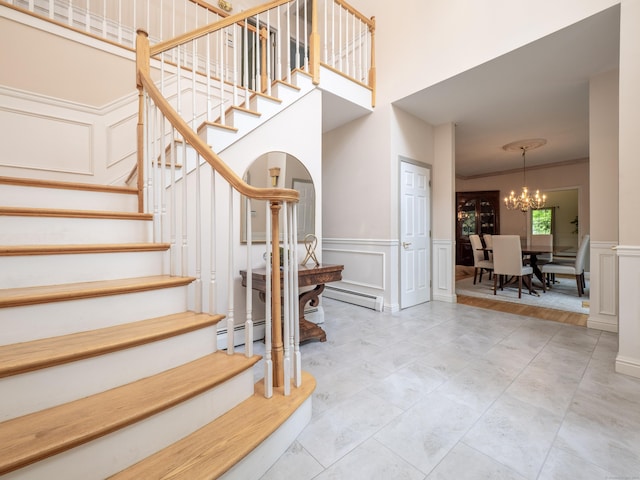 stairway featuring a decorative wall, a chandelier, a wainscoted wall, a baseboard heating unit, and ornamental molding
