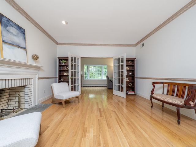 sitting room featuring wood finished floors, a brick fireplace, ornamental molding, baseboards, and a baseboard heating unit