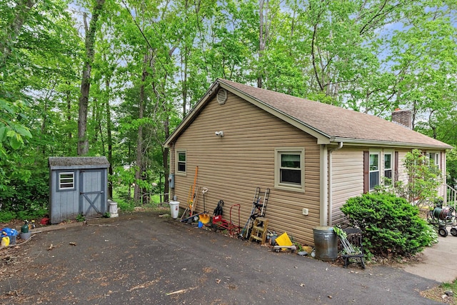 8 Sycamore Rd, East Lyme, CT 06357 - view of side of property with a storage unit, an outdoor structure, a chimney, roof with shingles, and view of wooded area