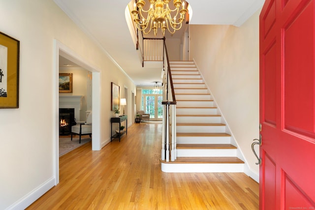 14 Fernhurst, Farmington, CT 06032 - foyer entrance featuring a chandelier, ornamental molding, stairway, light wood-style floors, and a warm lit fireplace