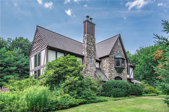 15 Tunxis Trl, Redding, CT 06896 - view of property exterior featuring a chimney, roof with shingles, a lawn, stone siding, and stucco siding