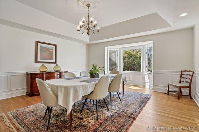 212 Fence Row Dr, Fairfield, CT 06824 - dining room with a decorative wall, a chandelier, light wood-style flooring, a tray ceiling, and wainscoting