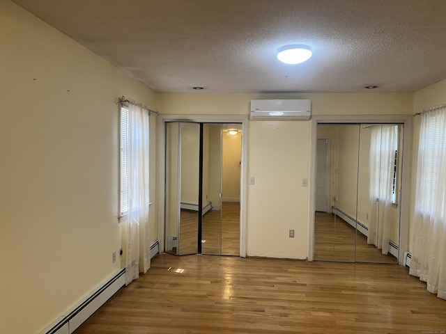 40 Bellevue Rd, New Haven, CT 06511 - unfurnished bedroom featuring a wall mounted air conditioner, two closets, a baseboard radiator, light wood-style flooring, and a textured ceiling
