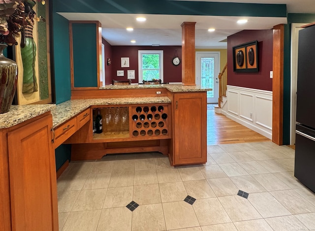 1 Russell Ln, Simsbury, CT 06070 - kitchen with brown cabinetry, a peninsula, a wainscoted wall, light tile patterned flooring, and light stone countertops