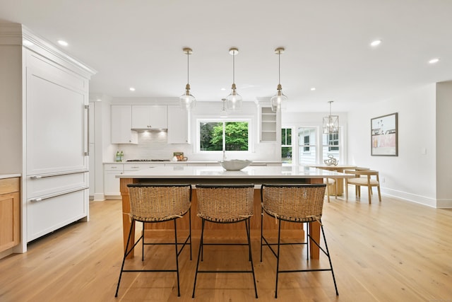 181 Highland Ave, Norwalk, CT 06853 - kitchen featuring decorative backsplash, light wood-type flooring, a kitchen breakfast bar, white cabinetry, and a kitchen island