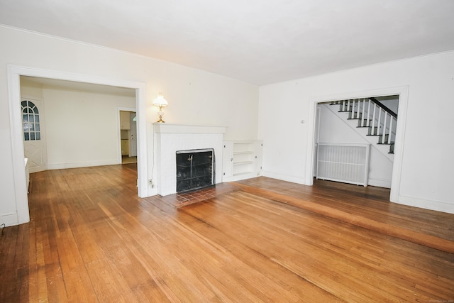 497 Commonwealth Ave, New Britain, CT 06053 - unfurnished living room featuring stairway, radiator heating unit, wood-type flooring, a brick fireplace, and baseboards