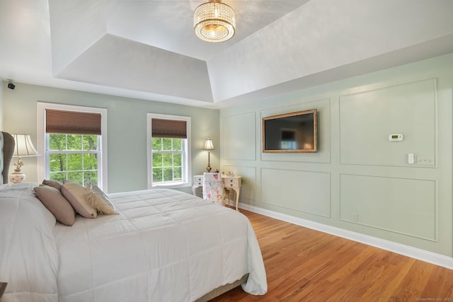 bedroom with light wood finished floors, a tray ceiling, and a chandelier