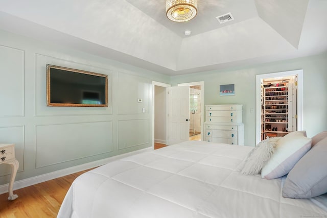bedroom with light wood-type flooring, a tray ceiling, connected bathroom, a walk in closet, and a closet