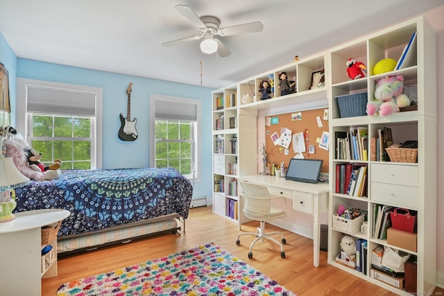 bedroom featuring wood finished floors, a desk, and baseboard heating