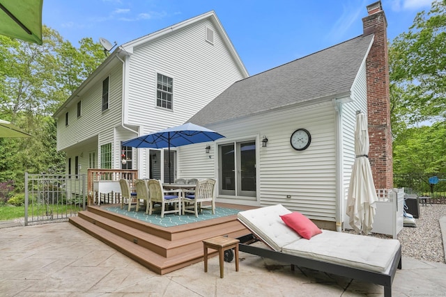 rear view of property with outdoor dining area, a chimney, a shingled roof, a deck, and a patio