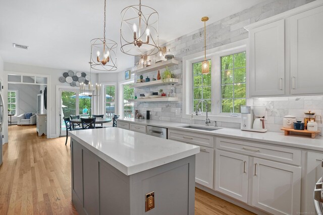 kitchen with a sink, a chandelier, dishwasher, a center island, and tasteful backsplash