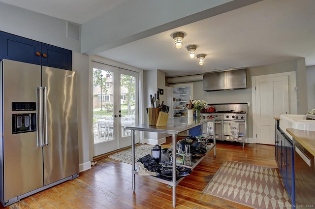 kitchen with high quality appliances, wall chimney range hood, blue cabinets, dark wood-type flooring, and french doors