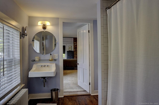 bathroom featuring radiator, wood finished floors, a sink, and baseboards