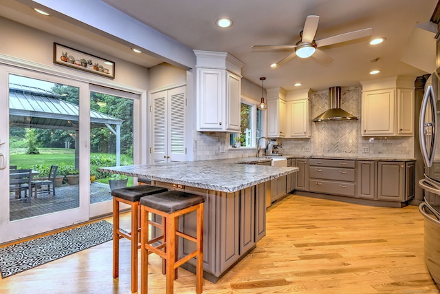 691 Buttonball Rd, Orange, CT 06477 - kitchen featuring wall chimney exhaust hood, a peninsula, light wood finished floors, a ceiling fan, and light stone counters