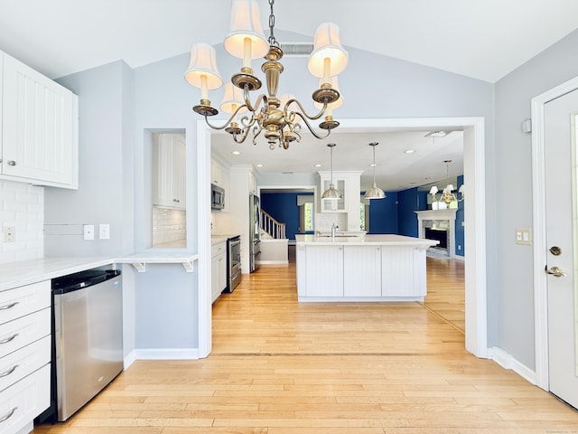 12 Rolling Ln, Norwalk, CT 06851 - kitchen featuring appliances with stainless steel finishes, a chandelier, a fireplace, tasteful backsplash, and light wood-type flooring