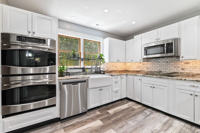 254 Haley Rd, Groton, CT 06355 - kitchen with appliances with stainless steel finishes, light stone counters, decorative backsplash, white cabinetry, and light wood-style floors