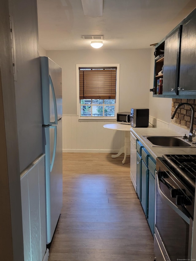 50 Greenhouse Rd Unit 41C, Bridgeport, CT 06606 - kitchen featuring a sink, light wood-type flooring, wainscoting, open shelves, and appliances with stainless steel finishes