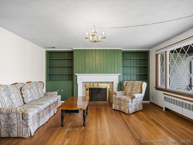 21 Poplar St, Enfield, CT 06082 - living room featuring radiator, built in features, a brick fireplace, a chandelier, and wood finished floors