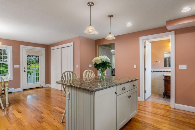 113 E Rd, East Windsor, CT 06016 - kitchen with light wood finished floors, hanging light fixtures, a kitchen island, white cabinets, and dark stone counters
