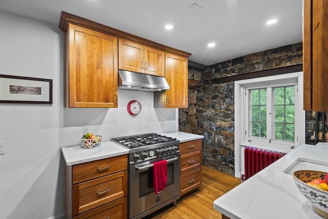 128 Blake Rd, Hamden, CT 06517 - kitchen with stainless steel range, under cabinet range hood, radiator heating unit, light wood-type flooring, and brown cabinets