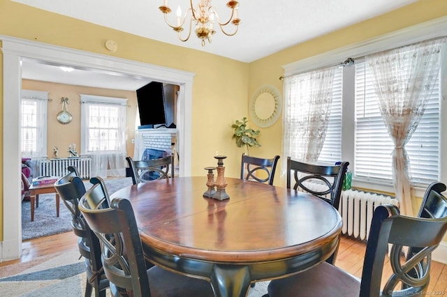 809 Burnside Ave, East Hartford, CT 06108 - dining space with radiator, a fireplace, light wood-style flooring, and a chandelier