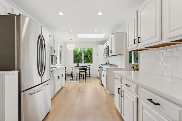 11 Valley Rd, Westport, CT 06880 - kitchen featuring stainless steel appliances, light wood-style flooring, a skylight, white cabinetry, and backsplash