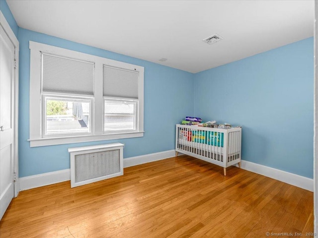 18 Geer Ave, Norwich, CT 06360 - bedroom with light wood-type flooring, baseboards, radiator heating unit, and a crib