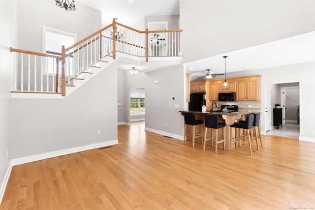 584 Meriden Ave Unit 1, Southington, CT 06489 - kitchen with black appliances, a breakfast bar, light brown cabinetry, light wood-style flooring, and baseboards