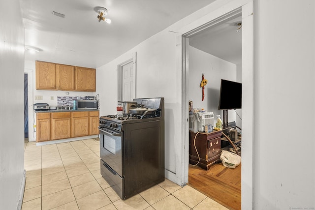 171 Frank St, New Haven, CT 06519 - kitchen with black gas range oven, stainless steel microwave, light tile patterned floors, brown cabinetry, and dark countertops
