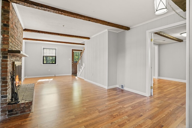 1975 Huntington Rd, Stratford, CT 06614 - unfurnished living room with wood finished floors, beam ceiling, a brick fireplace, stairs, and ornamental molding