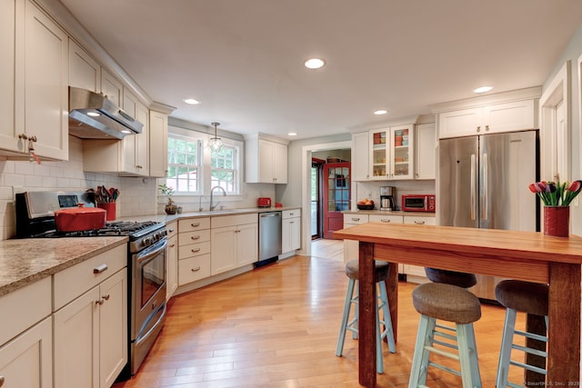 96 Middle Haddam Rd, East Hampton, CT 06456 - kitchen with under cabinet range hood, stainless steel appliances, a sink, light wood finished floors, and backsplash