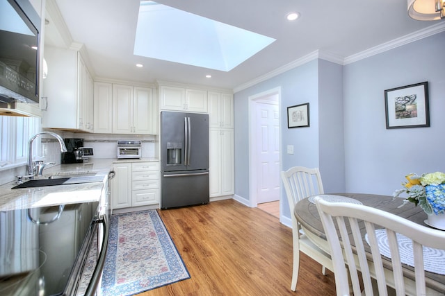 85 Oakridge Rd, Trumbull, CT 06611 - kitchen with stainless steel fridge with ice dispenser, a sink, a skylight, white cabinets, and light wood-type flooring