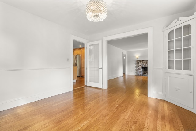 10 Paddock Pl, Milford, CT 06461 - spare room with a chandelier, a stone fireplace, light wood-style flooring, and baseboards