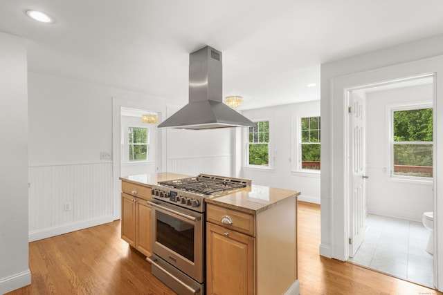 10 Paddock Pl, Milford, CT 06461 - kitchen with stainless steel stove, island range hood, light wood-type flooring, a wainscoted wall, and light stone counters
