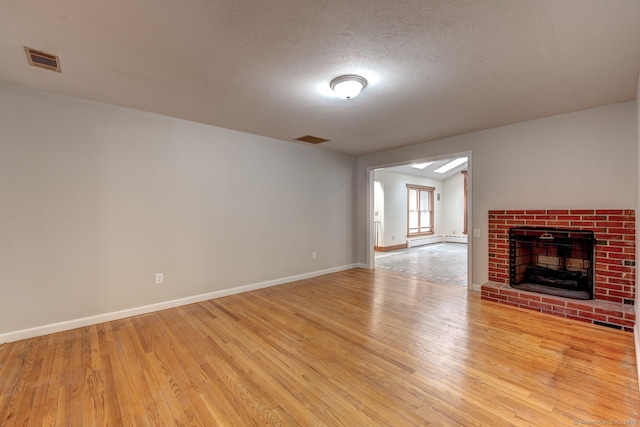 3 Clear View Dr, Mansfield, CT 06250 - unfurnished living room featuring light wood-type flooring, baseboard heating, baseboards, a brick fireplace, and a textured ceiling