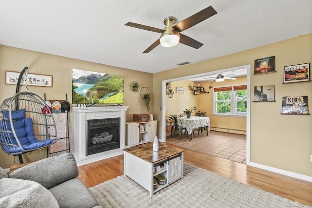 96 Flanders River Rd, Coventry, CT 06238 - living room with a baseboard heating unit, a ceiling fan, light wood-style floors, and a fireplace