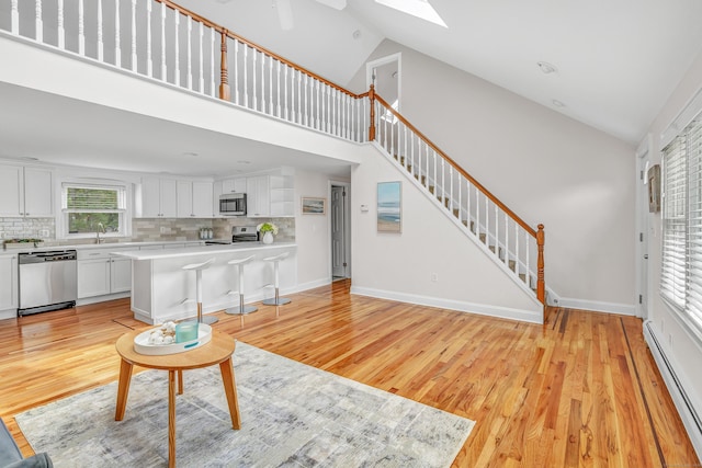5 Wildmere Ln, Norwalk, CT 06851 - living area featuring baseboard heating, light wood-type flooring, a skylight, stairway, and high vaulted ceiling
